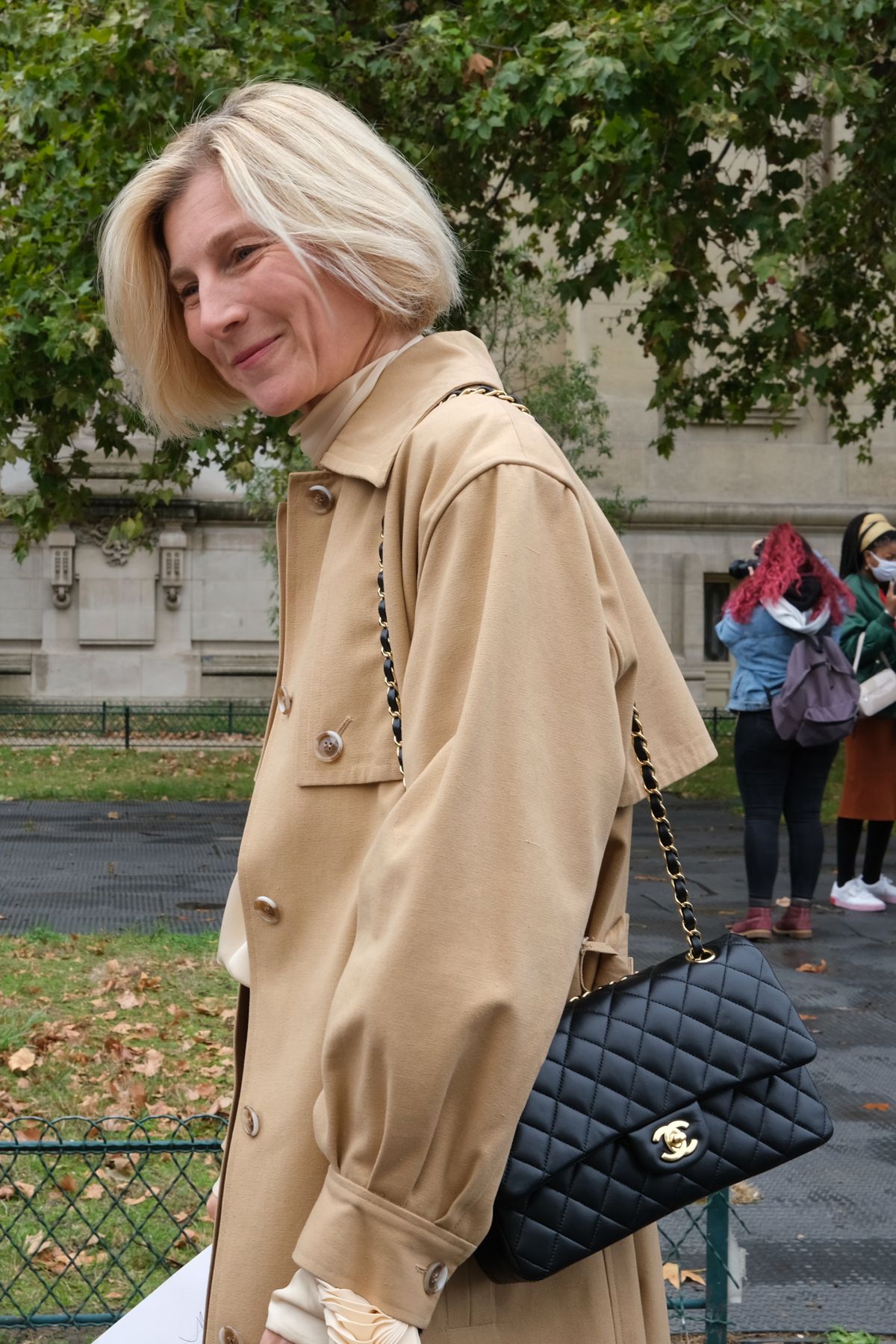 Woman with Trench Coat and Black Chanel bag attending Chanel SS21 Show in Paris